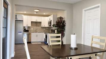 Una cocina moderna con armarios blancos, una mesa de comedor con sillas y una planta en maceta.