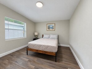 A bedroom with a bed, a nightstand, a lamp, a window with blinds, and a ceiling light. - vacation home close to the beach (Clearwater)