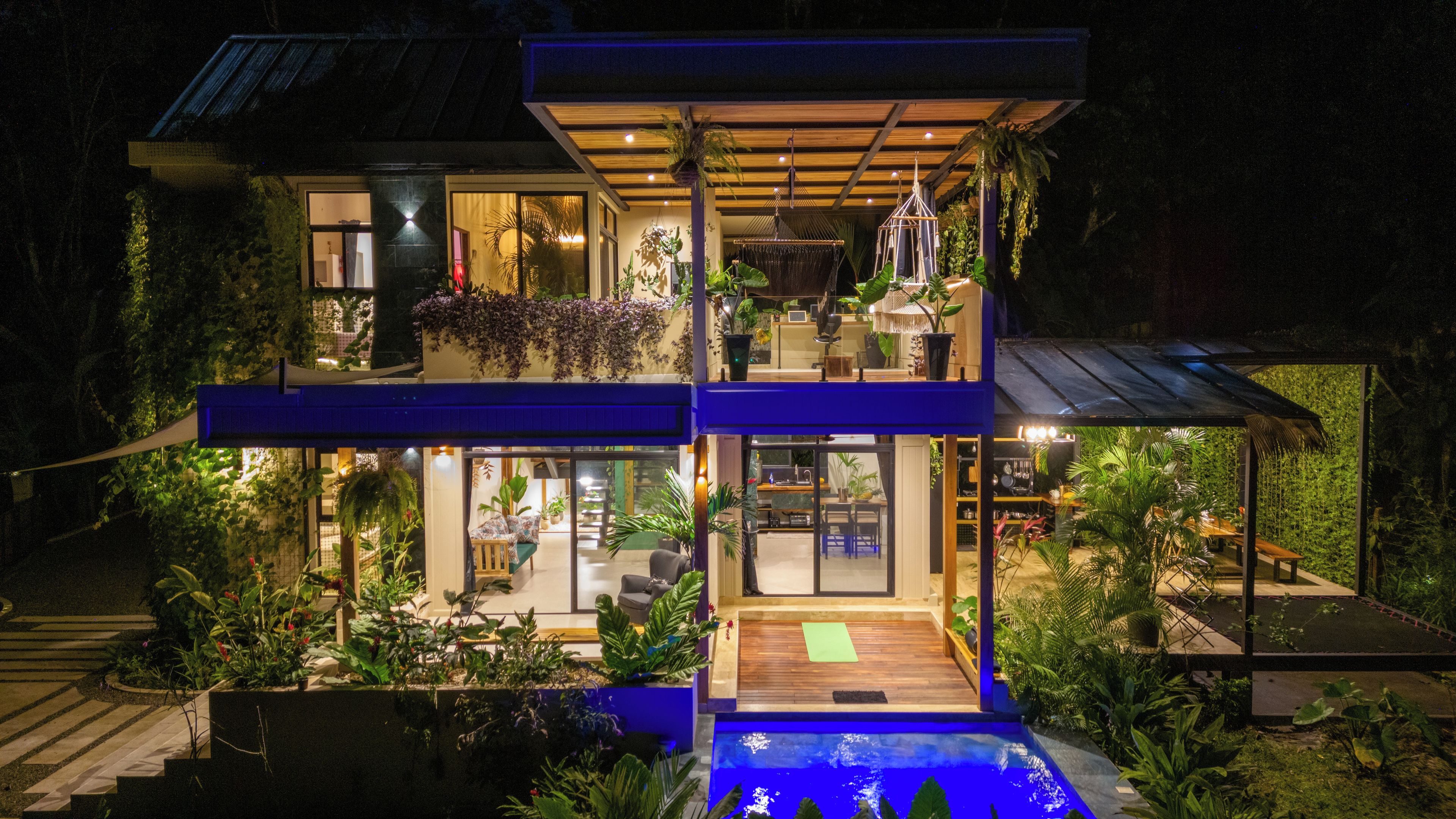 A modern two-story house with a swimming pool, outdoor seating, and lush greenery.