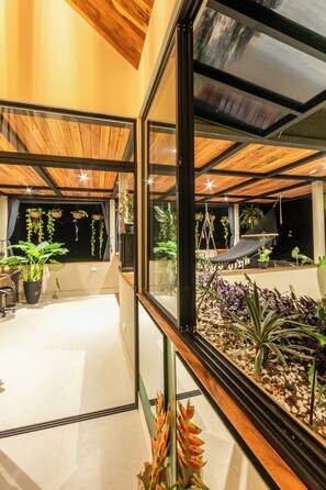 A modern interior with a large glass window, wooden ceiling, and various potted plants. - Con Amor Caribe · 2,500 sq ft · Jungle Villa · Wildlife at Your Door ·Near Beach (Manzanillo)