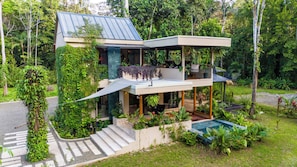 Ein modernes, zweistöckiges Haus mit überdachter Terrasse, umgeben von üppigem Grün.