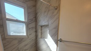 Um chuveiro com paredes de mármore, uma pequena janela e um chão de azulejos de pedra.