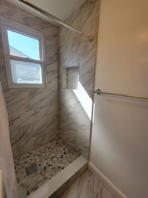 Eine Dusche mit Marmorwänden, einem kleinen Fenster und einem Steinfliesenboden.