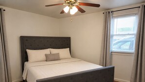 Un dormitorio con cama, ventilador de techo y ventana con cortinas.