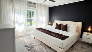 Un dormitorio con cama, ventilador de techo, mesita de noche y ventana con cortinas.