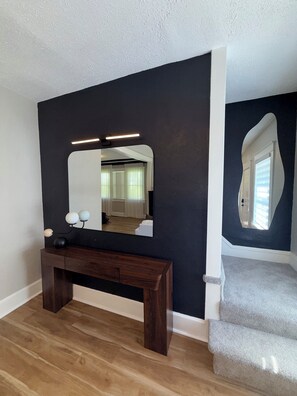 A room with a dark wall, a wooden console table, a mirror, and a staircase. -     Fully Remodeled 3Bed- 2 Bath  Home  Ideal for Extended Stays (Kansas City)