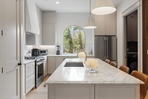 A modern kitchen with a large island, stainless steel appliances, and a view through a large window. - Relaxing Estate - Heated Pool - Near UT & Moody Center (Austin)