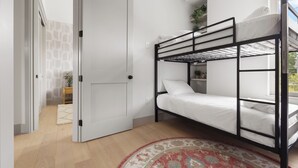 Una habitació amb un llit superposat, una porta, una taula petita amb una planta i una catifa estampada.