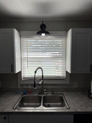 A kitchen with a double sink, a window with blinds, and a pendant light.