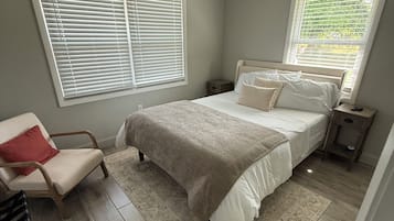 A bedroom with a bed, a chair, a nightstand, a ceiling fan, and large windows.