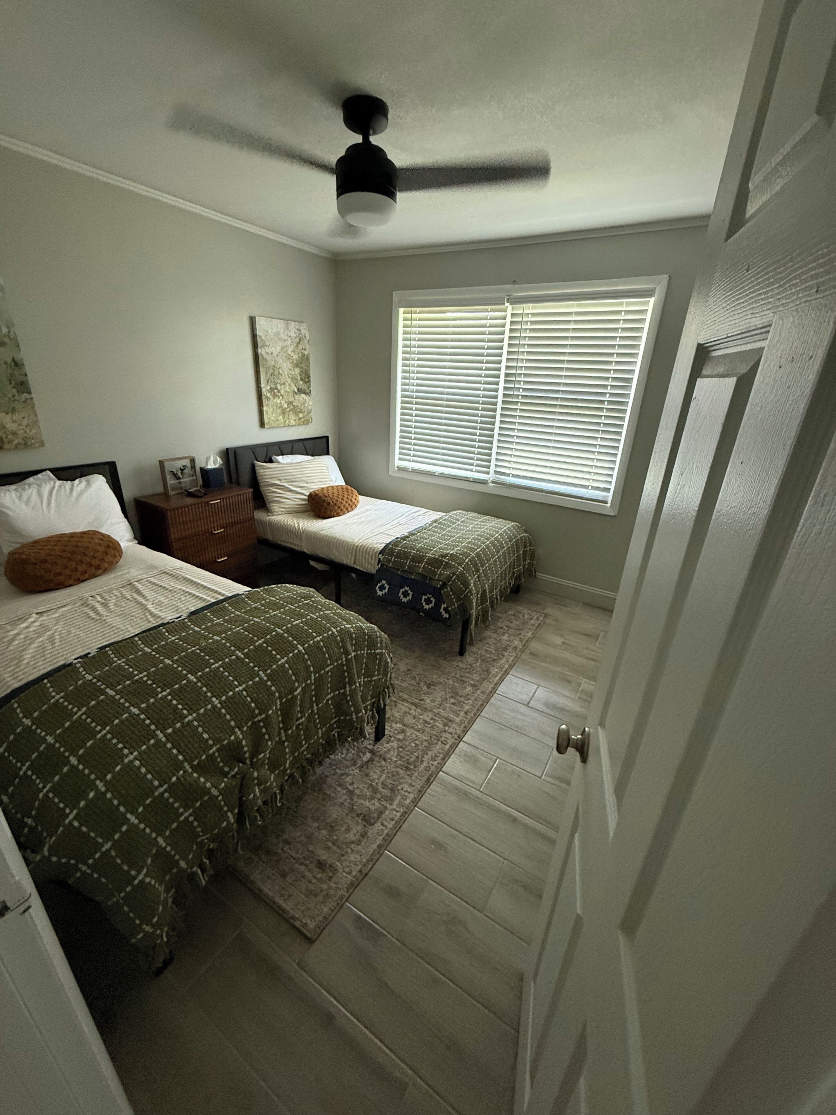 Ein Schlafzimmer mit zwei Betten, einem Deckenventilator, einem Fenster mit Jalousien und einer Tür.
