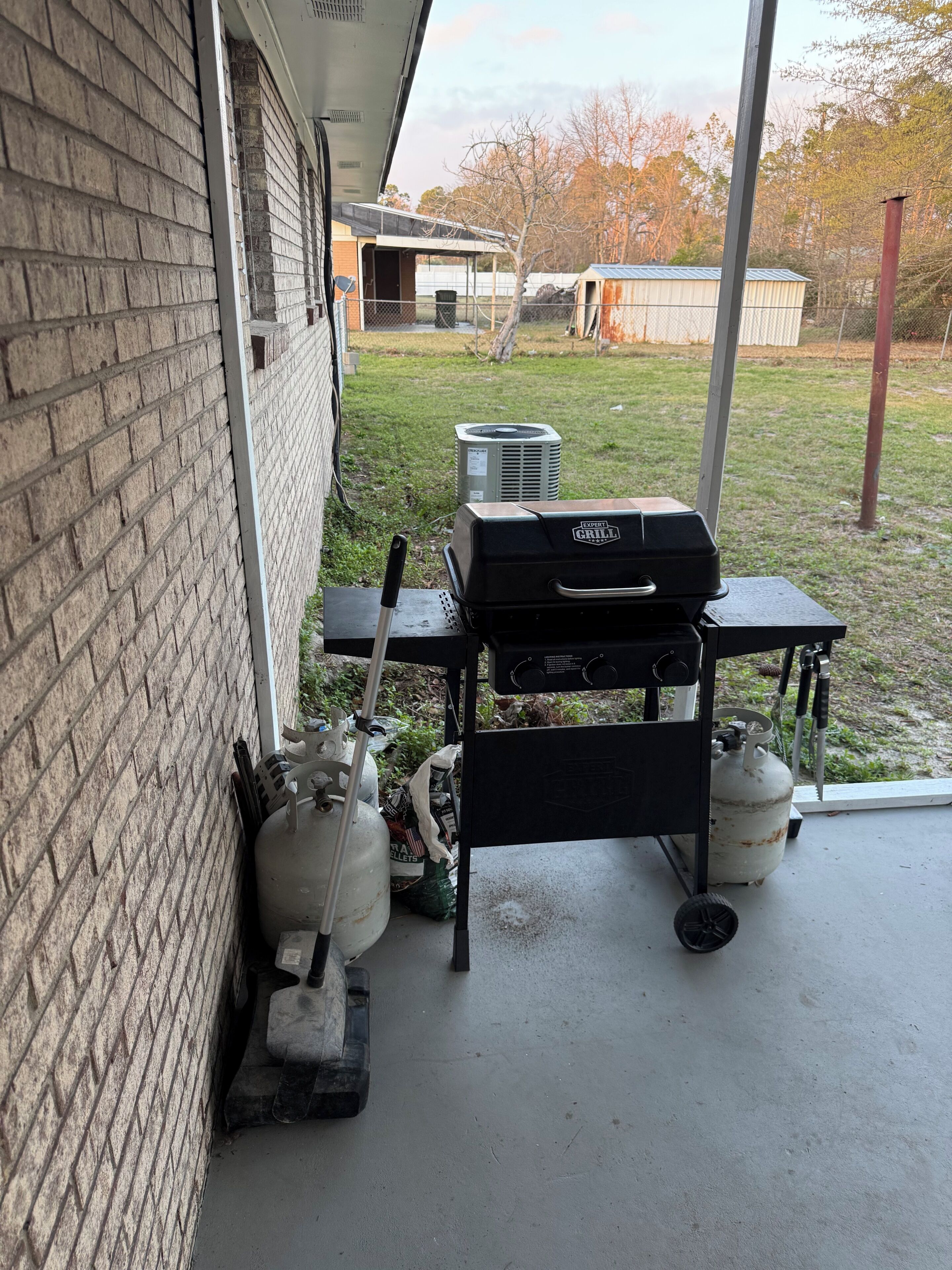 A patio area with a grill, propane tanks, and a brick wall.