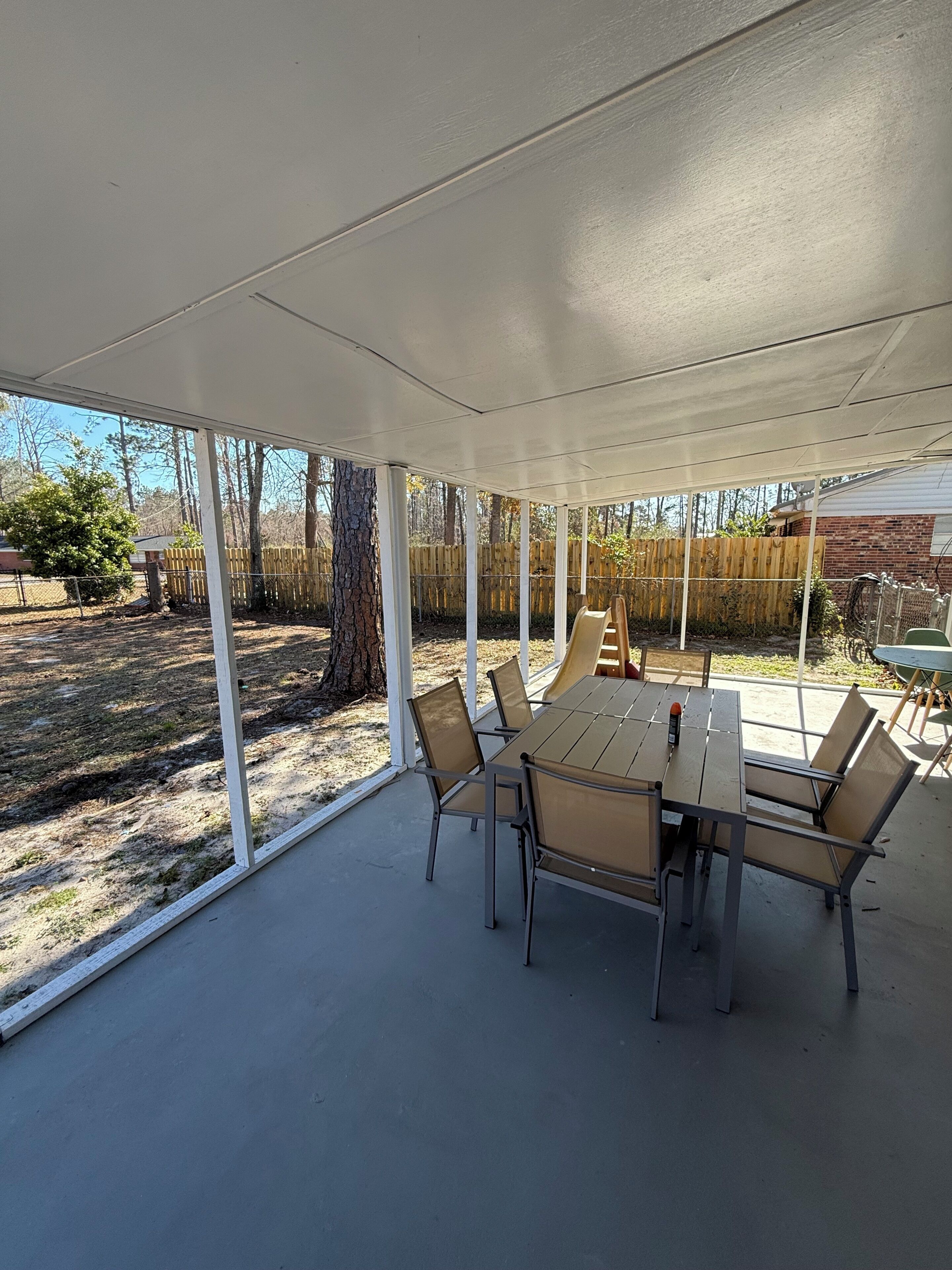 A covered patio area with a table and chairs, surrounded by a wooden fence and trees.