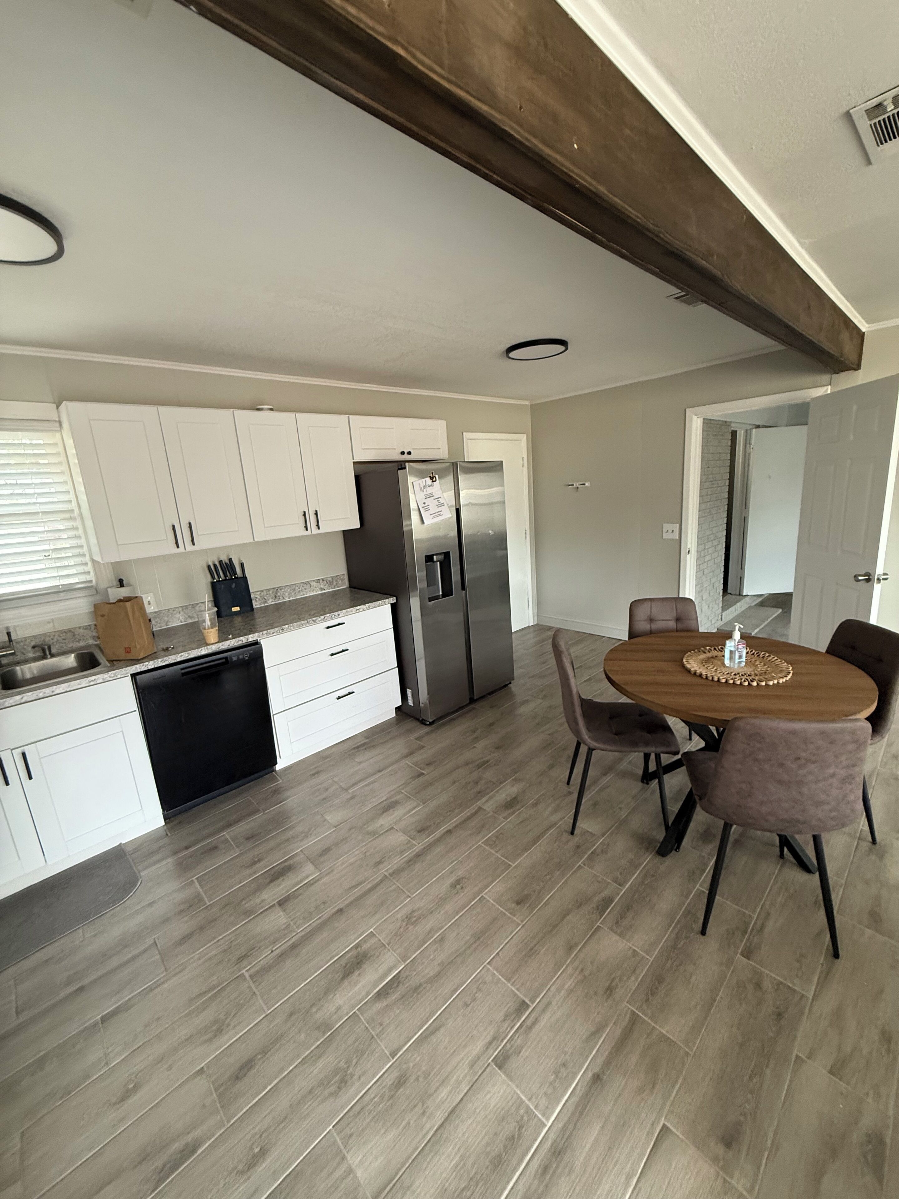 Une cuisine moderne avec des meubles blancs, un réfrigérateur en acier inoxydable et un coin repas comprenant une table et des chaises en bois.