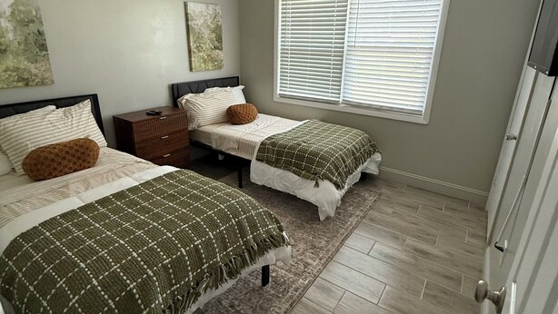 Een slaapkamer met twee bedden, een plafondventilator, een raam met jaloezieën en een houten vloer.