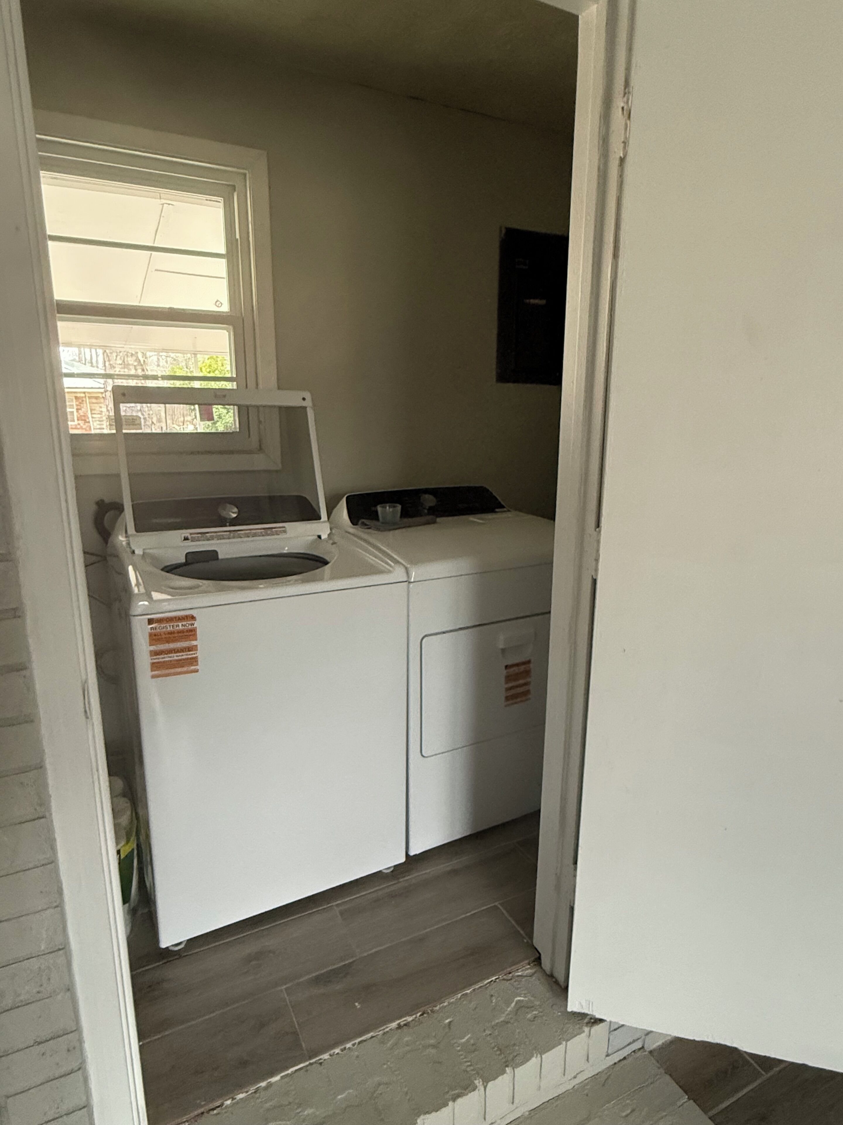 A laundry room with a washing machine and dryer, a window, and a door leading to another room.