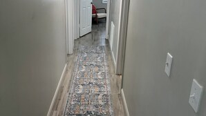Een gang met een kamerbreed tapijt, houten vloeren en witte wanden.