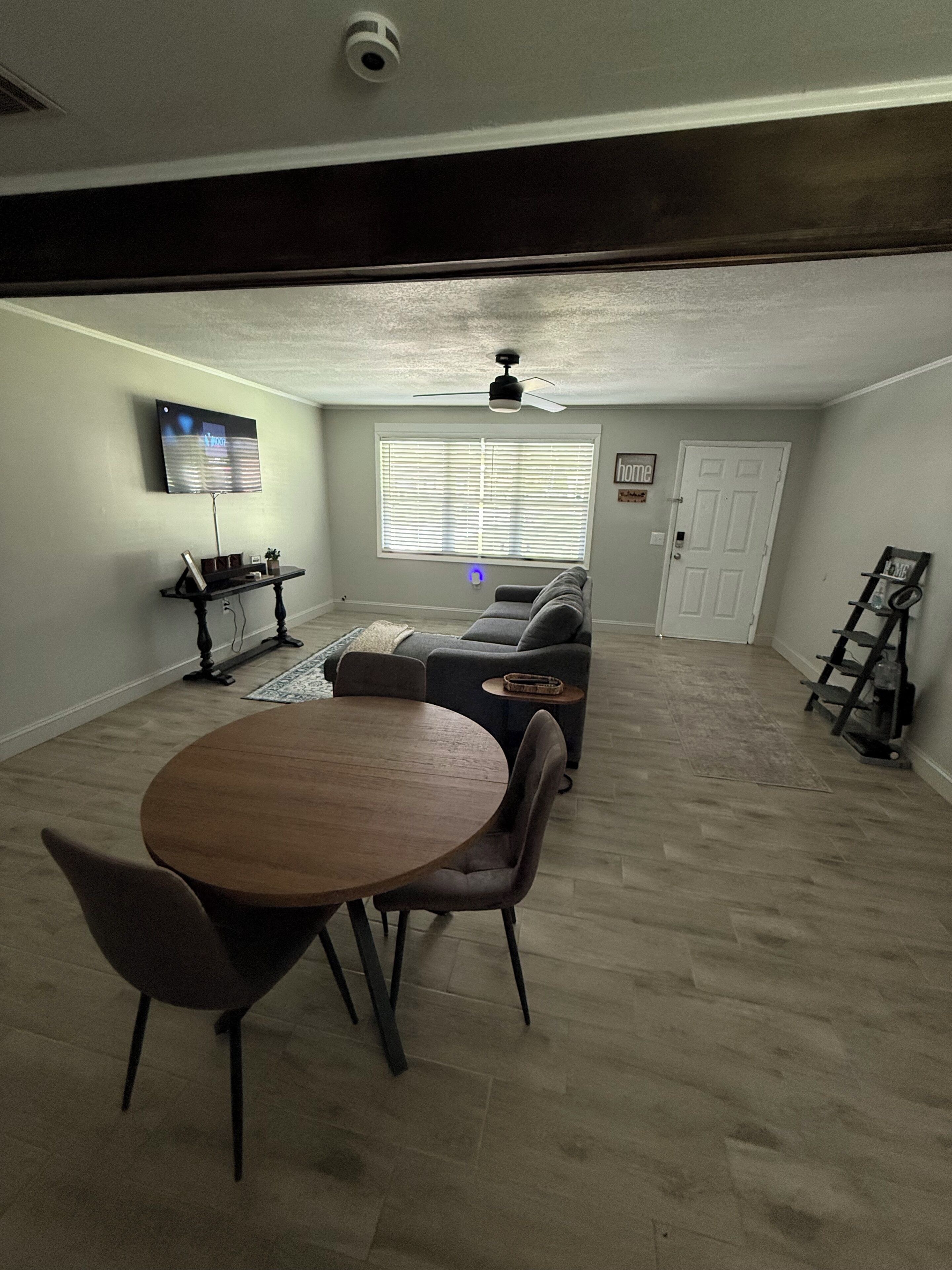Een kamer met een eettafel, stoelen, een bank, een televisie en een plafondventilator.