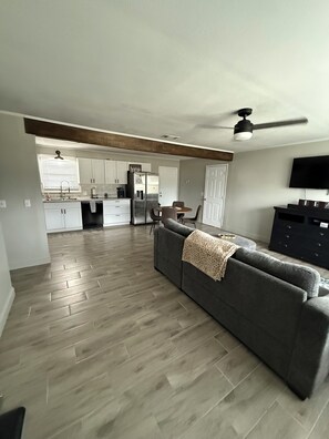 A spacious living area with a grey sofa, a dining table, and a kitchen in the background.