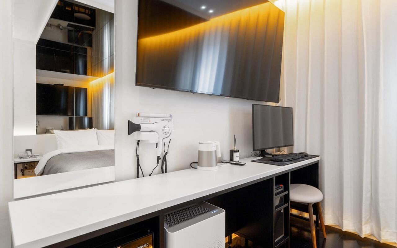Habitación de hotel moderna con un televisor de pantalla plana grande montado en la pared, un escritorio con computadora, cafetera y una silla.