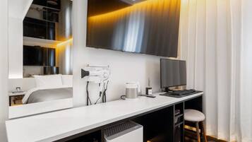 Habitación de hotel moderna con un televisor de pantalla plana grande montado en la pared, un escritorio con computadora, cafetera y una silla.