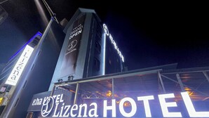 Une enseigne d’hôtel indiquant « EL Lizena HOTEL » et une tour sur laquelle on peut lire « GRAND OPENING » (grande ouverture).