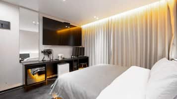 Habitación de hotel moderna con cama, escritorio, silla, televisor de pantalla plana y un ventanal con cortinas.