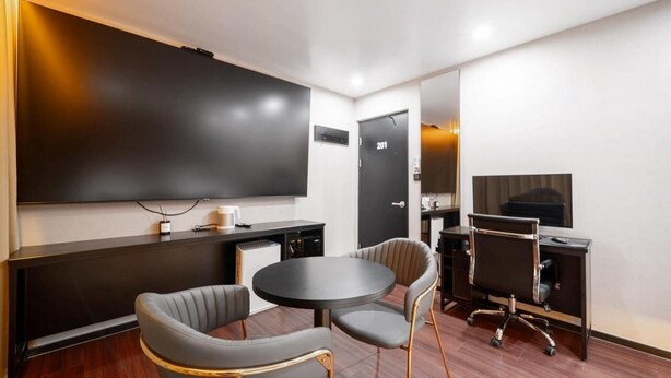 A conference room with a large flat-screen TV, a round table, two chairs, a desk, and a door marked '201'. - Lizena HOTEL (Asan)