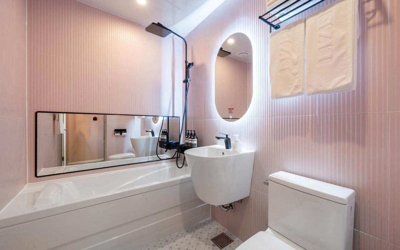 Un baño moderno con bañera, lavamanos, inodoro, cabezal de ducha, espejo y toalleros.