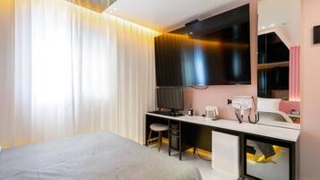 A modern hotel room with a bed, a desk with a computer, a mirror, and a television.