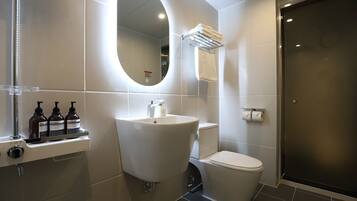 Une salle de bain moderne avec un grand miroir ovale, un lavabo sur colonne, des toilettes et un espace douche.