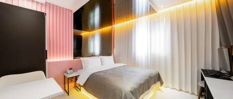 Una habitación de hotel moderna con cama, mesita de noche, escritorio y un gran ventanal con cortinas.