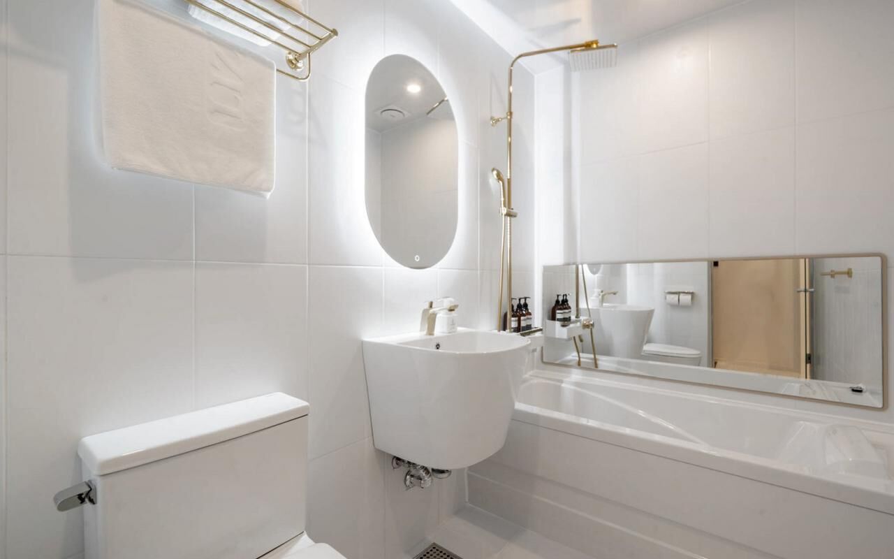 A modern bathroom with a toilet, sink, and bathtub, featuring a large mirror and gold fixtures.