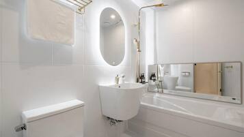 A modern bathroom with a toilet, sink, and bathtub, featuring a large mirror and gold fixtures.