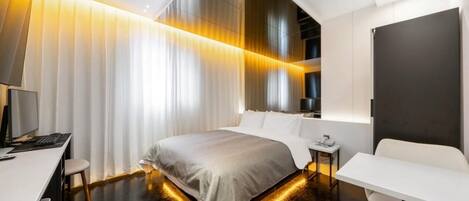Una habitación de hotel moderna con una cama grande, un escritorio, una silla y una mesita de noche.
