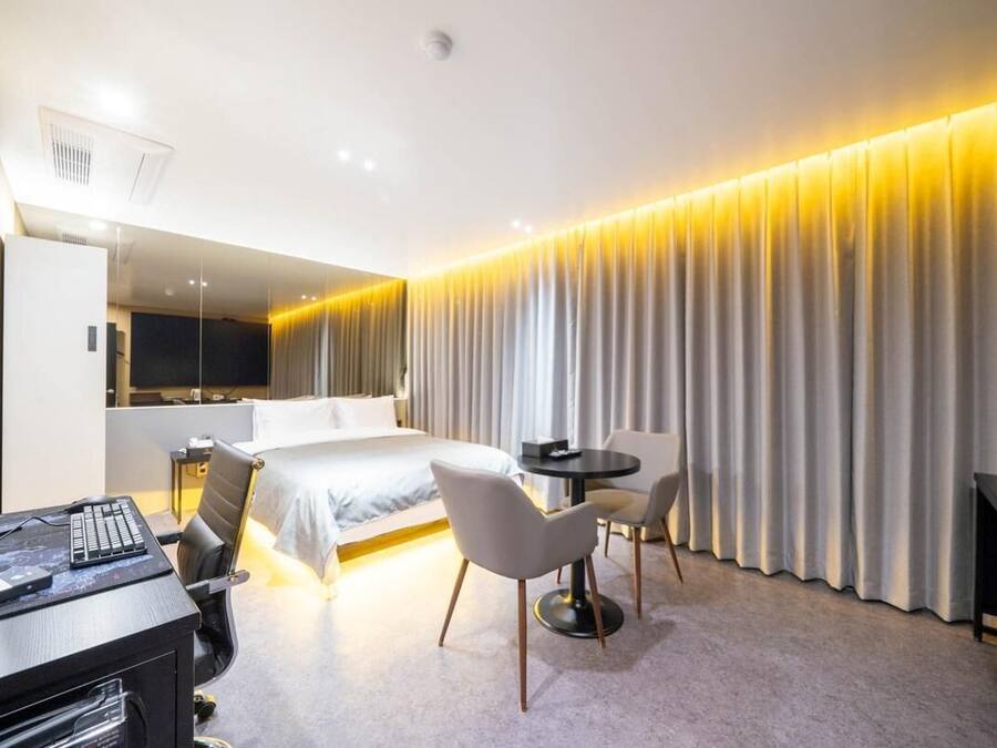 A hotel room with a bed, desk, chairs, and a TV.