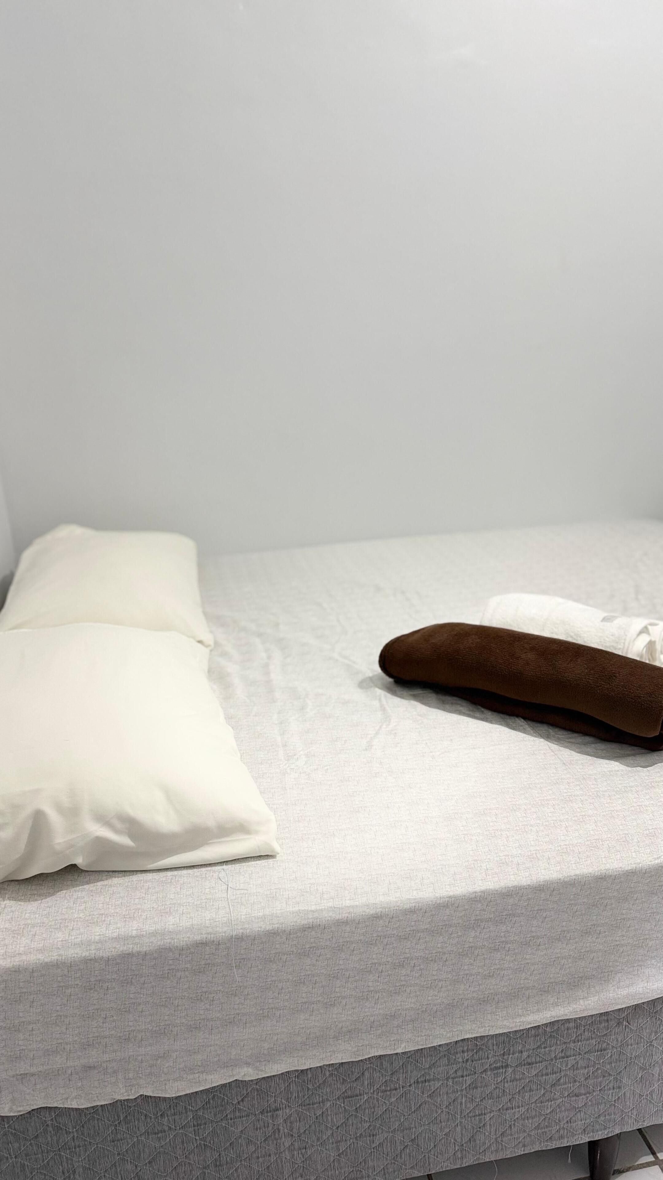 A bed with a grey quilted mattress, two pillows, and a brown pillow.