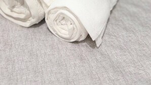 Una tovallola blanca doblegada amb cura i una tovallola marró sobre una superfície rugosa, probablement un llit o un escorredor de tovalloles.