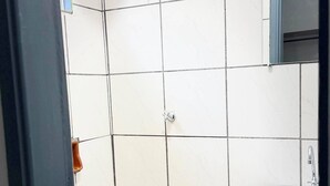 Un bany amb rajoles blanques, dutxa, rentapel i porta.