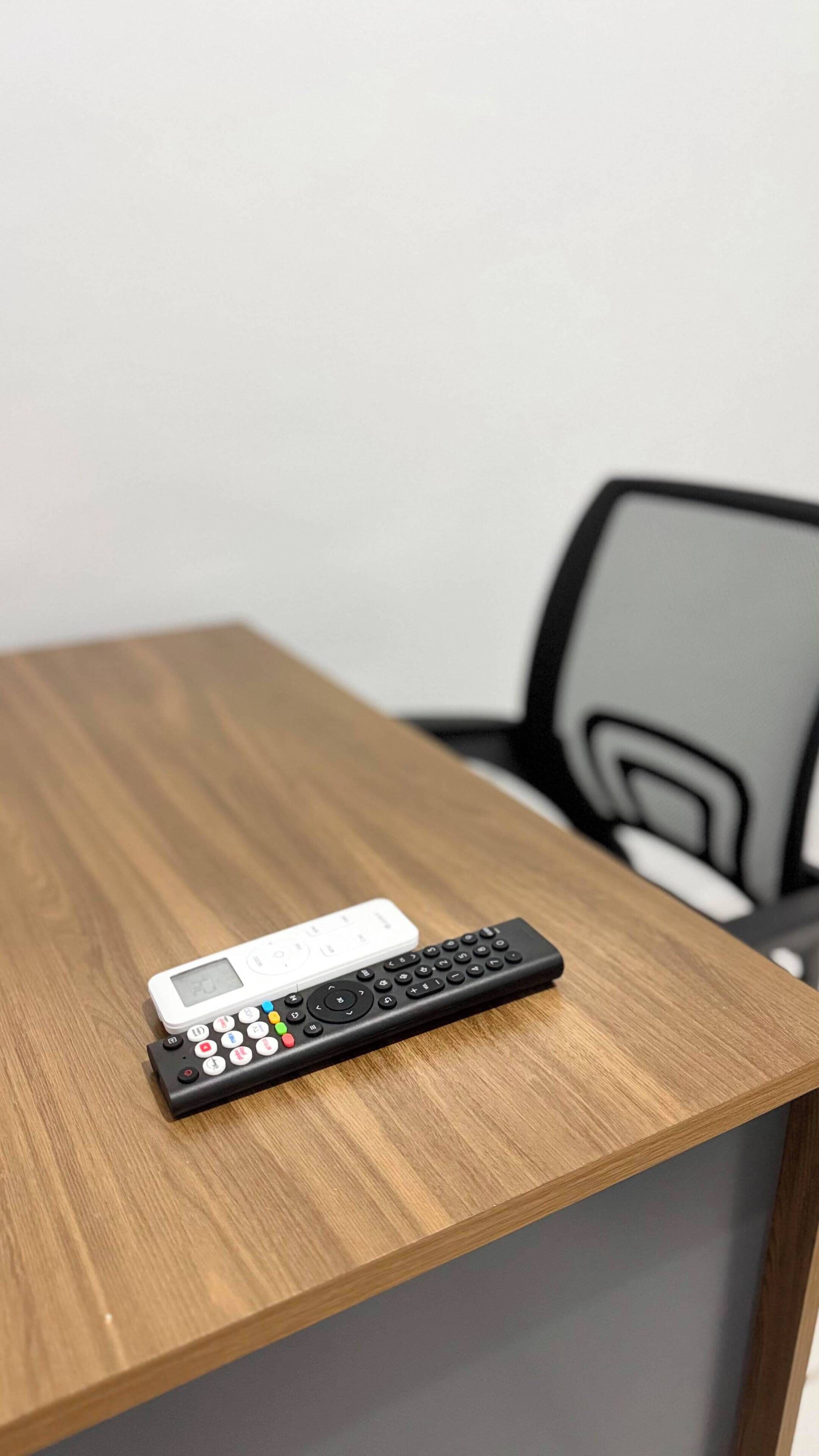 Uma mesa de madeira com um controle remoto preto e um controle remoto branco sobre ela.