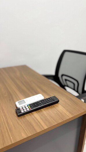 A wooden table with a black remote control and a white remote control on it. - Pousada Gente Feliz (Apiacás)