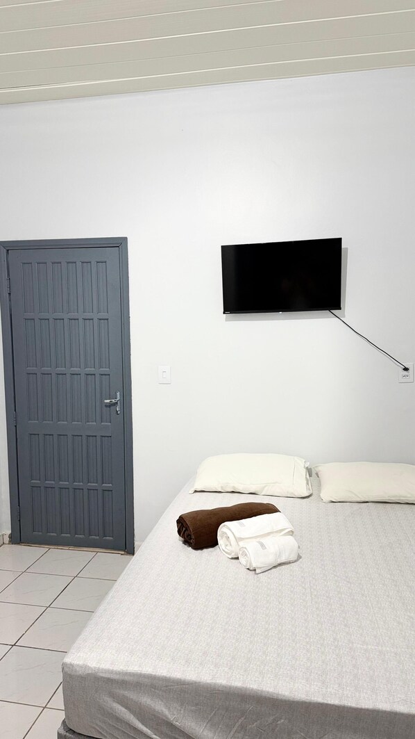 A room with a bed, a flat-screen TV mounted on the wall, and a door. - Pousada Gente Feliz (Apiacás)