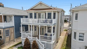 A two-story house with a balcony, a front porch, and a small front yard with two pine trees. - Pet Friendly/ Top-Floor 3BR Retreat -Near Beach & 34th St (Ocean City)