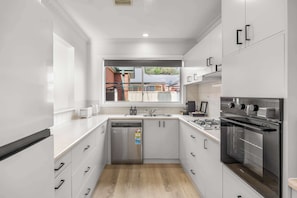 Una cocina moderna con electrodomésticos de acero inoxidable, lavavajillas y ventana con vista a un barrio residencial.