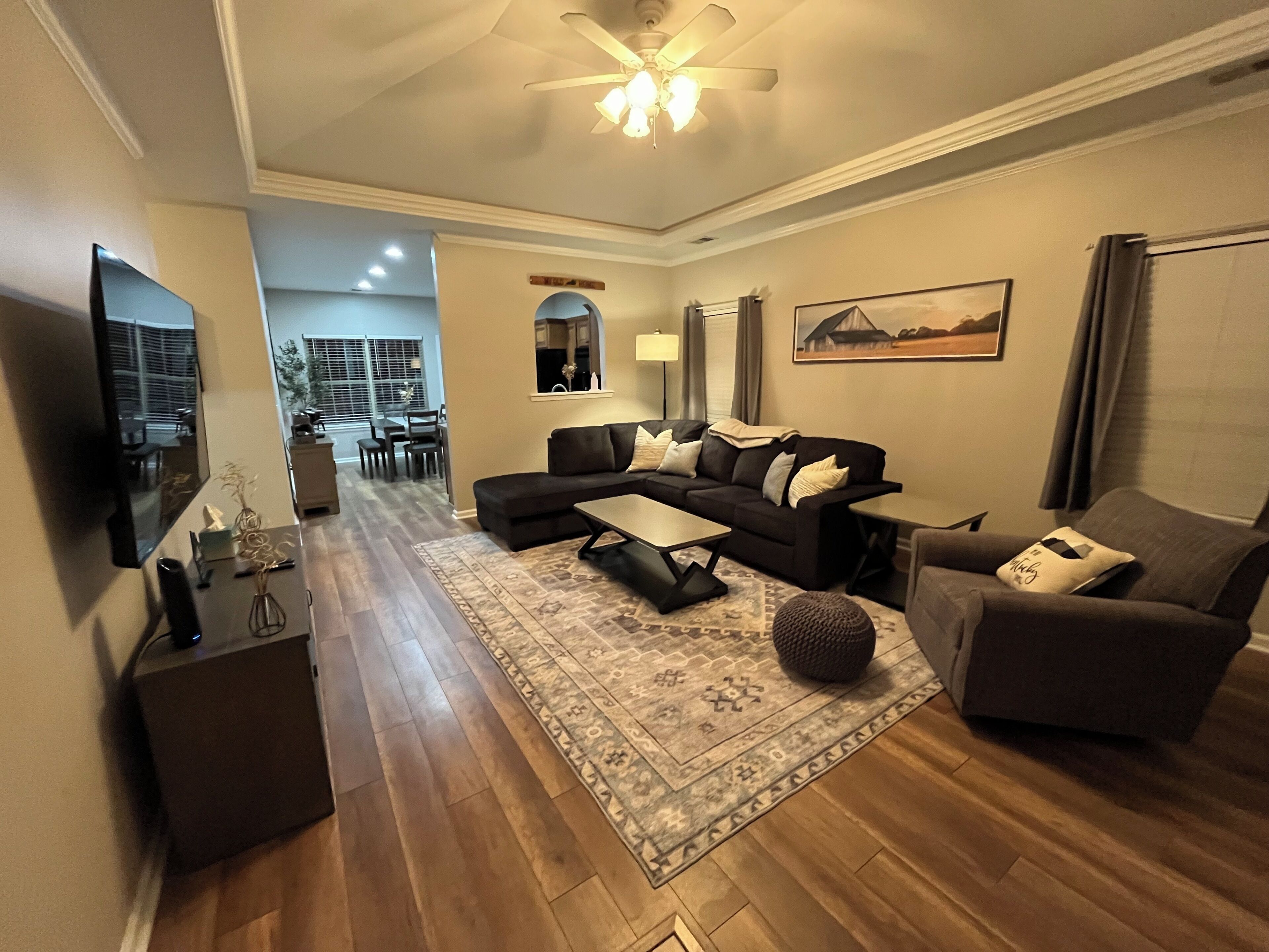 A modern living room with a sectional sofa, a coffee table, and a TV. There is a dining area in the background with a table and chairs.