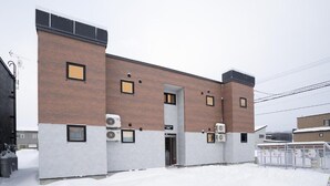 A building with a brick facade, multiple air conditioning units, and a gated entrance. - Niseko Town Retreat Amber (Abuta-gun, Kutchan-cho)