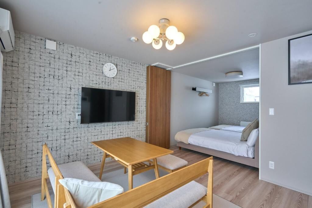 Una habitación moderna con pared de ladrillo, un televisor de pantalla plana, una mesa de madera con bancos, una cama y una ventana.