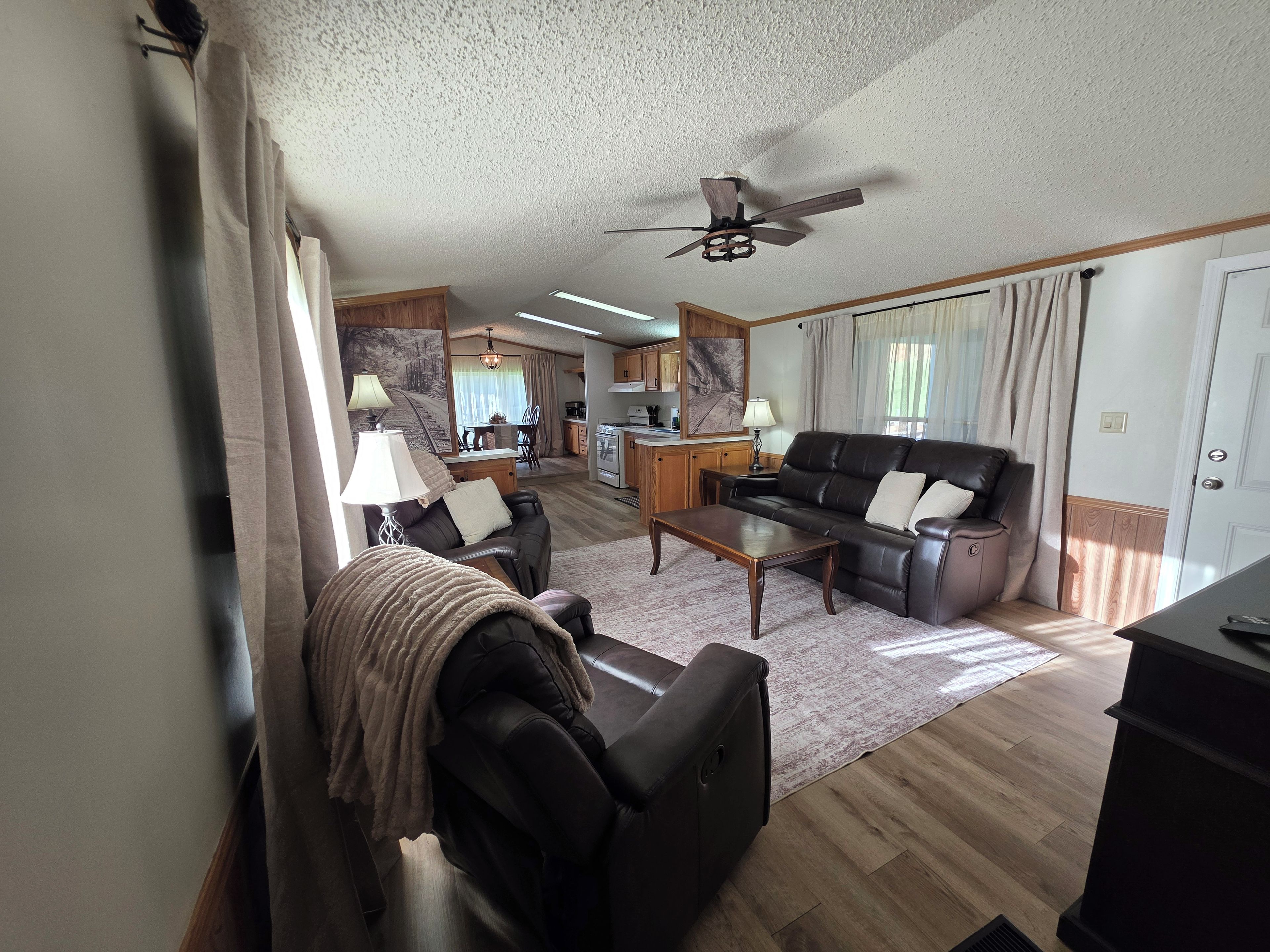 A living room with a sofa, armchair, coffee table, and a ceiling fan.