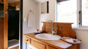 A bathroom with a wooden vanity, a sink, a towel rack, and a window providing natural light. - River Haven Experience ultimate luxury in our cabin. (Whakamārama)