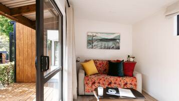 A modern living room with a wooden floor, a glass door, a sofa with colorful cushions, a painting on the wall, and a small table with a candle.